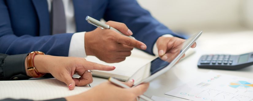 unrecognizable-business-people-sitting-at-meeting-with-charts-looking-and-pointing-at-tablet
